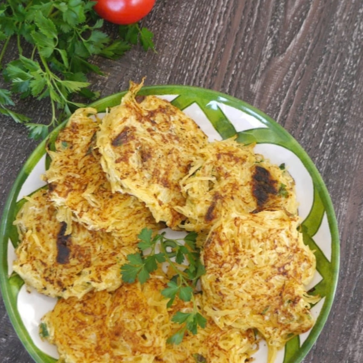 Spaghetti squash fritters on a green and white plate with fresh parsley