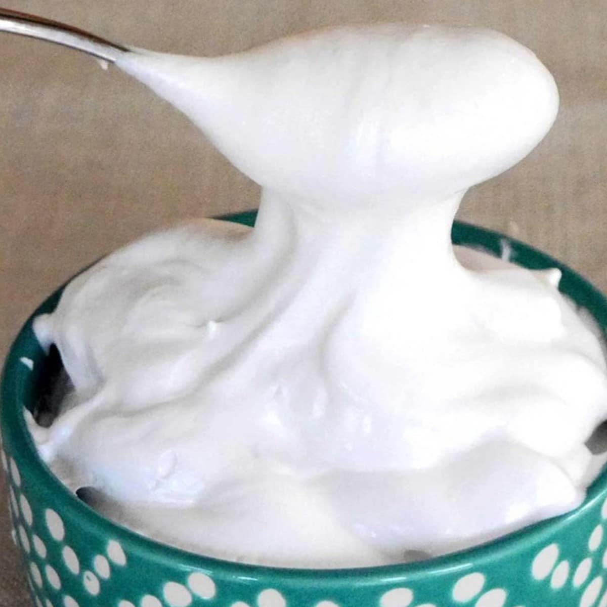 Sugar free marshmallow fluff on a spoon over a green polka dot bowl