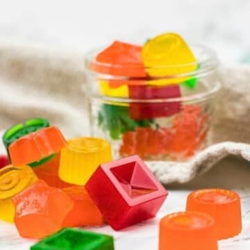 Colorful zero carb gummy candies in a glass jar and scattered on a marble counter