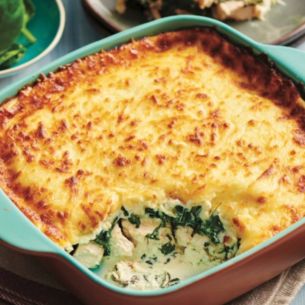 Keto creamy chicken spinach bake with a golden mozzarella top in a teal baking dish