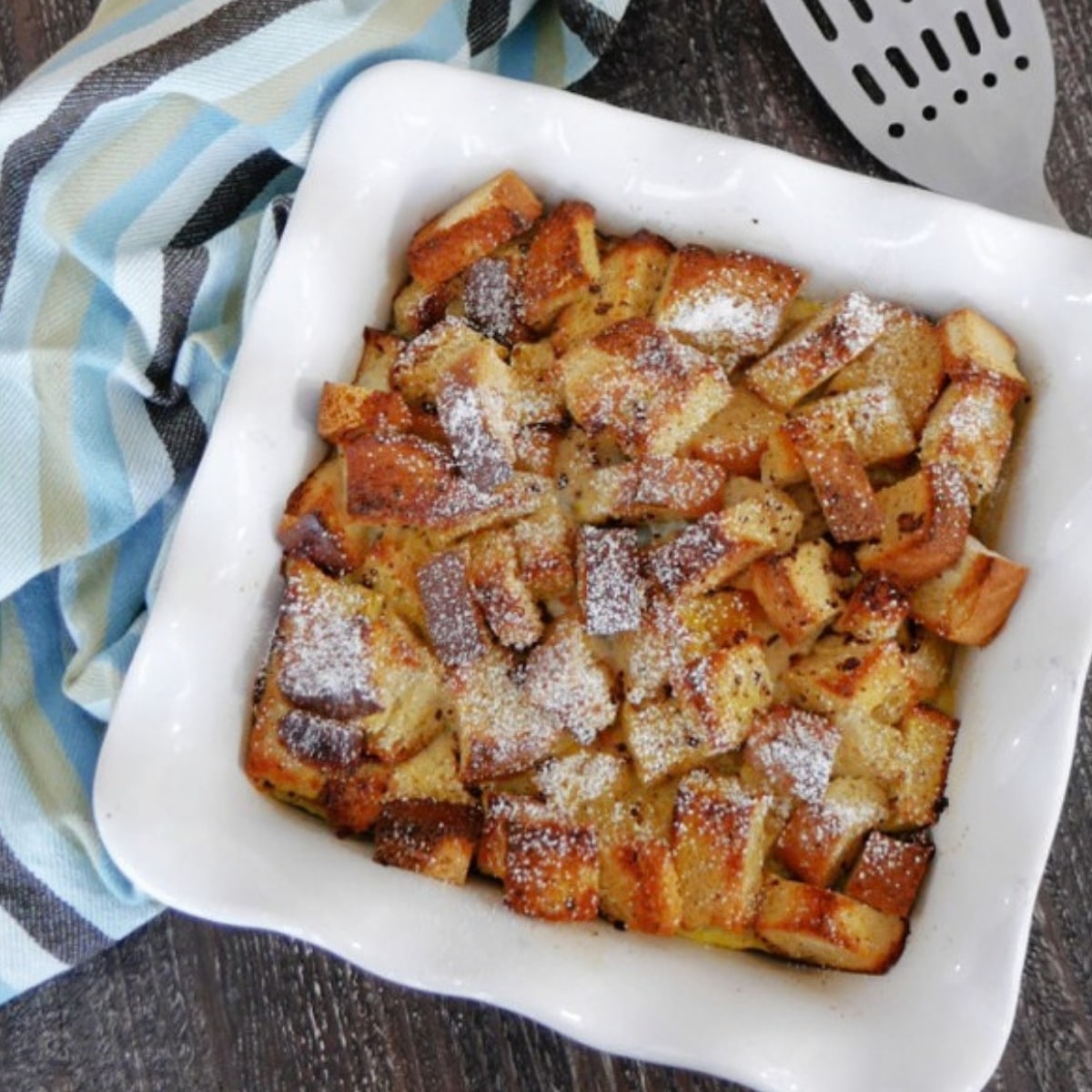 Keto French toast casserole in a white square baking dish dusted with powdered sweetener