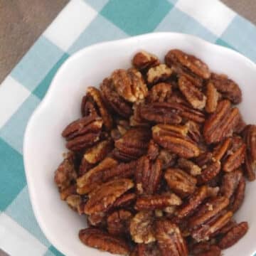 Low carb caramelized pecans in a white bowl on a teal gingham napkin
