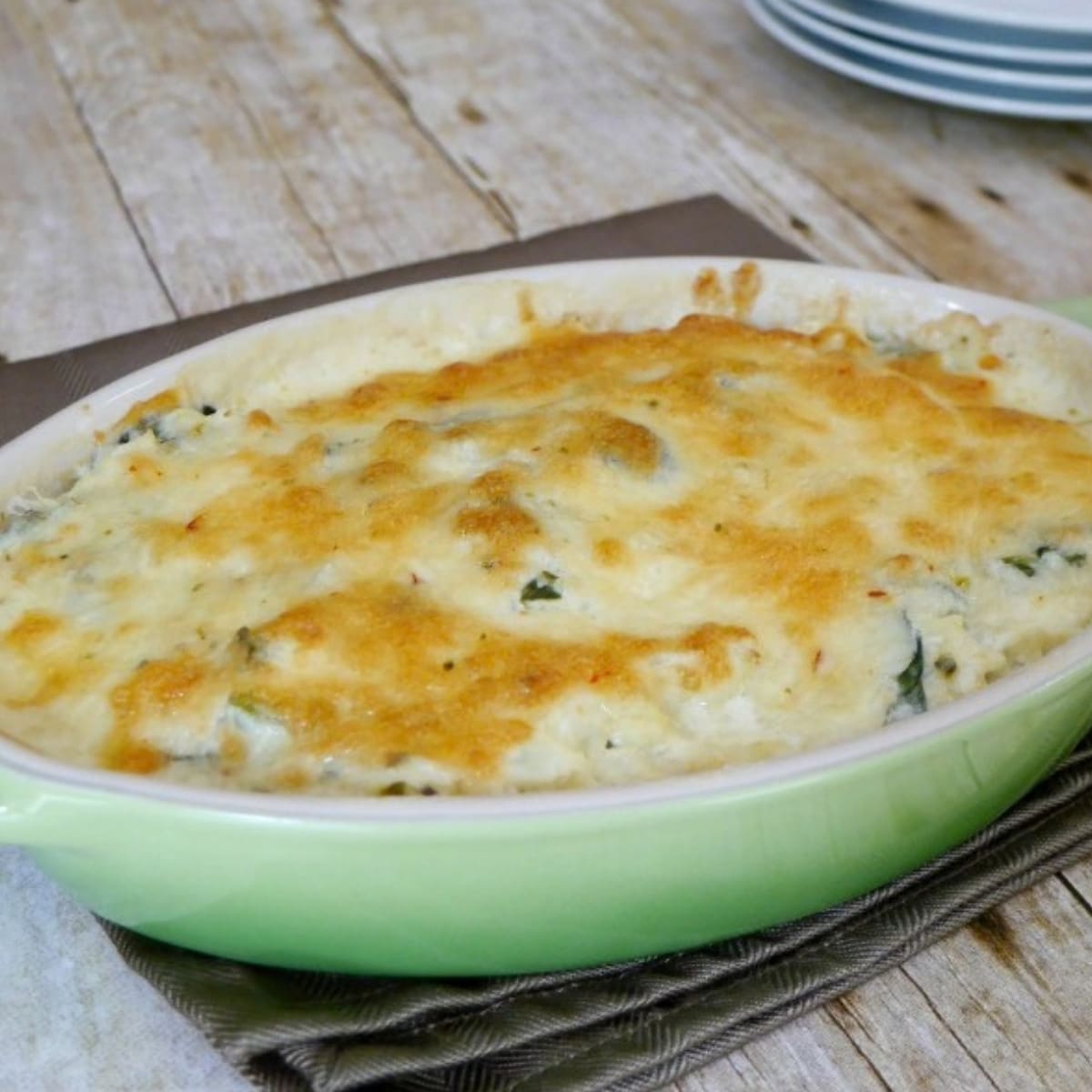 Low carb spinach cauliflower casserole with a golden cheese topping in a green oval baking dish