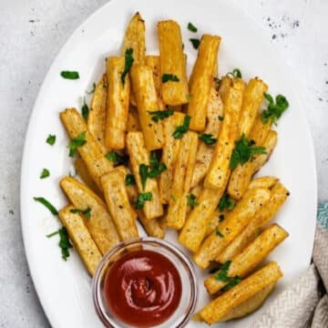 Low carb turnip fries on a white plate with fresh parsley and a small bowl of ketchup