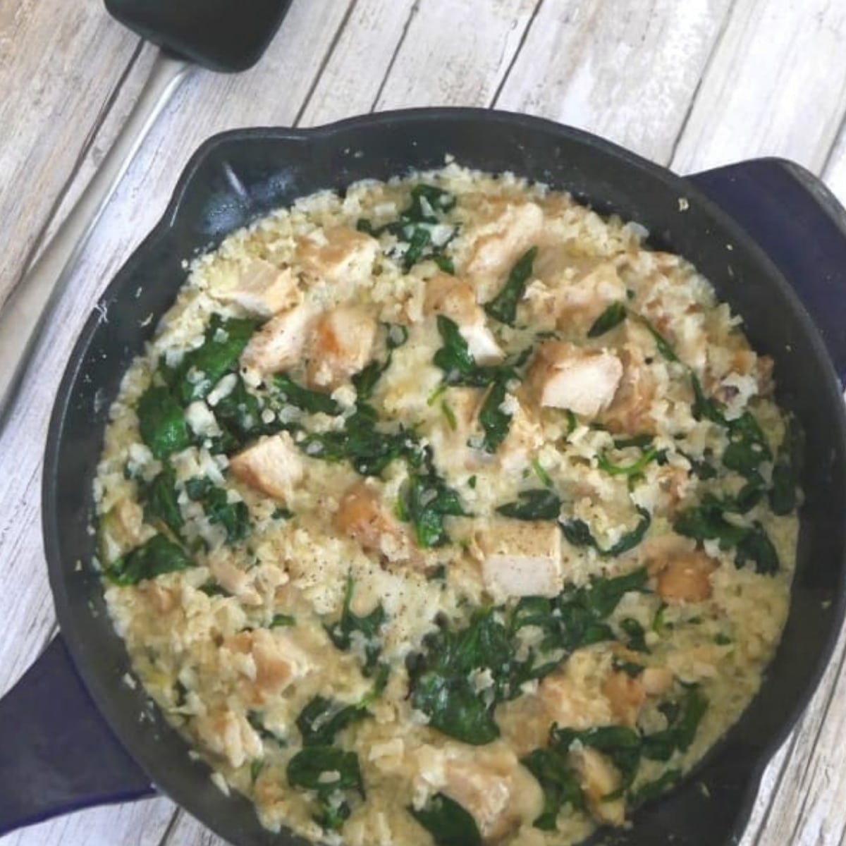 One pot chicken and cauliflower rice casserole with spinach in a blue cast iron skillet